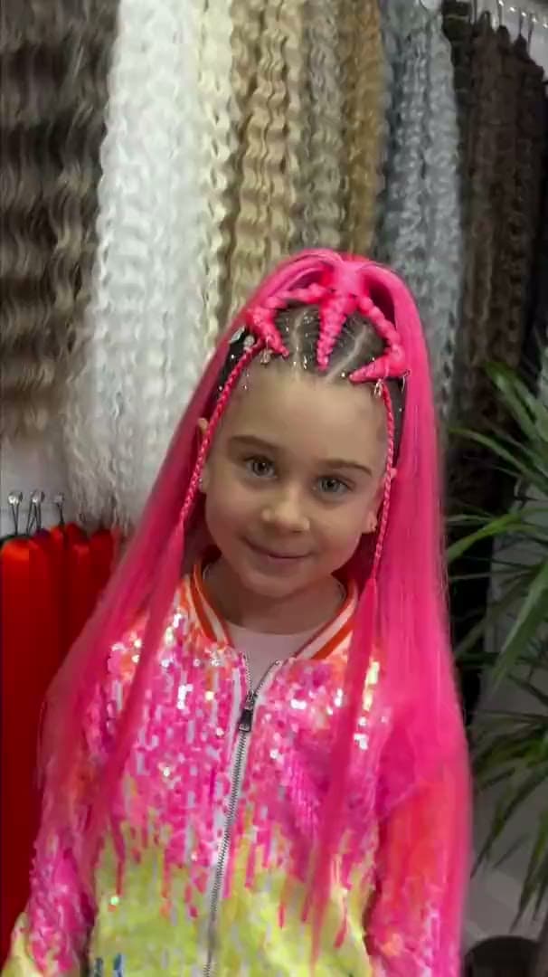 A child in bright pink braids, in front of the studio's wall of colour samples